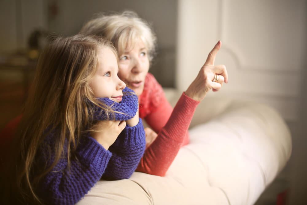Older woman sitting with child on couch pointing.